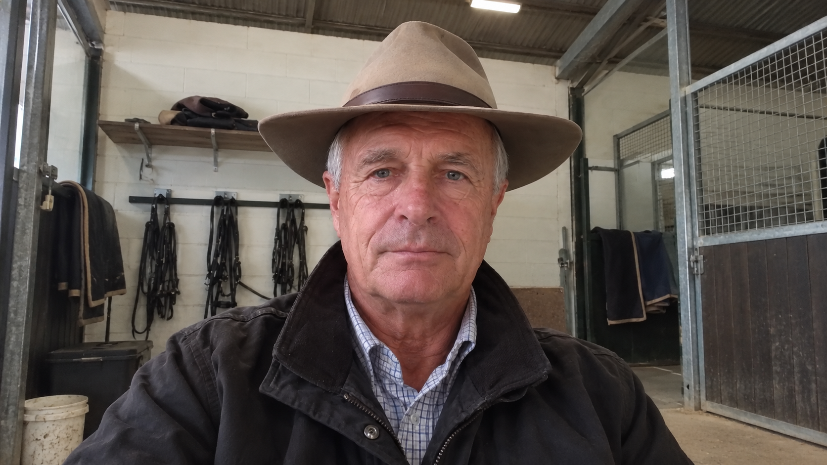 Frank wearing a broad-brimmed hat and dark jacket in a tack room